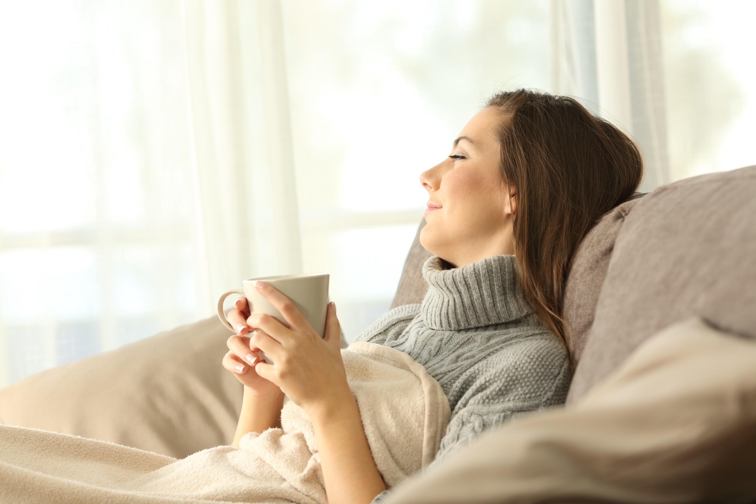 Woman in a cozy sweater relaxing on a couch with a cup of tea, a serene moment after acupuncture therapy for headache relief.