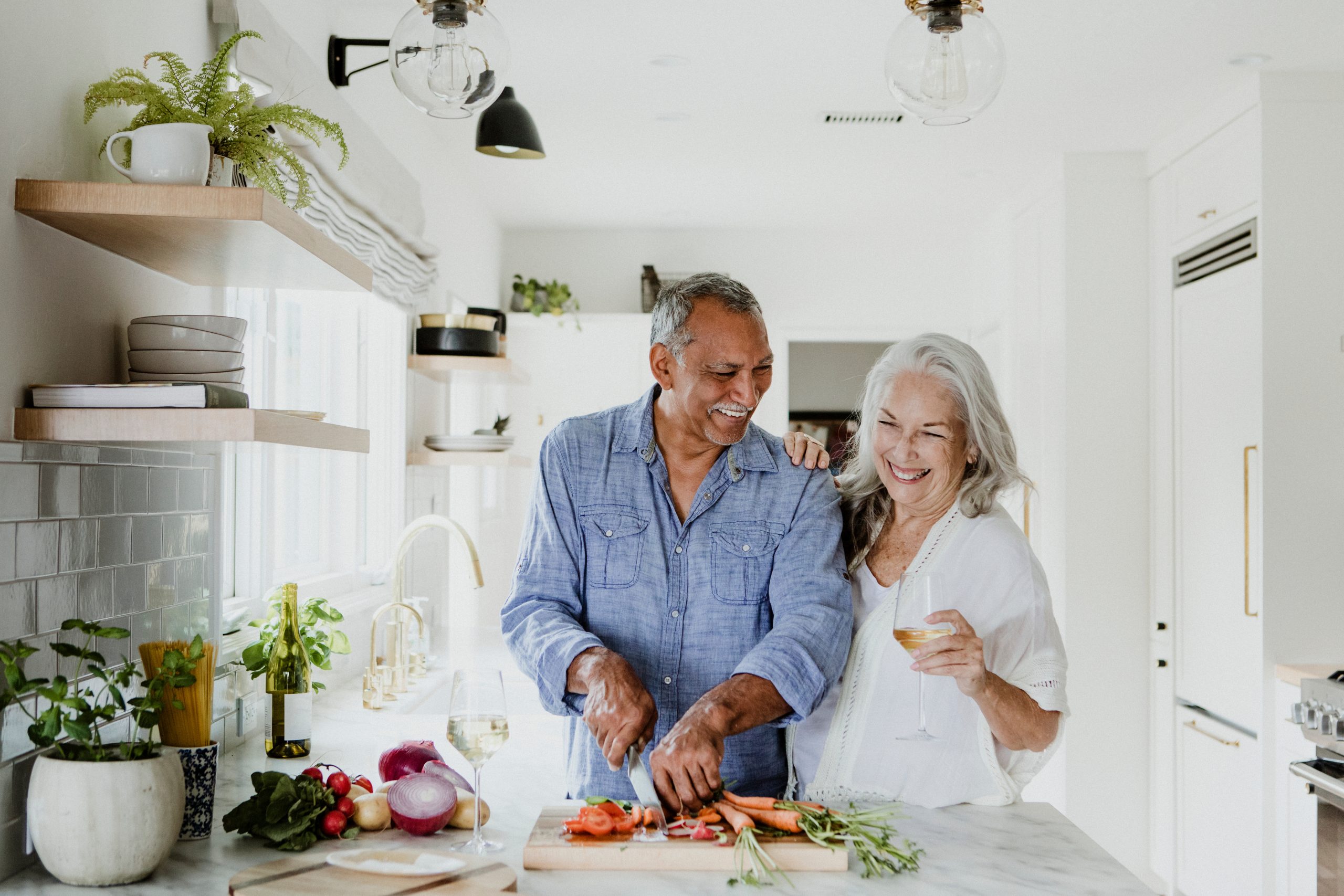 Senior couple laughing together while preparing a healthy meal in a bright kitchen, enjoying life without headache worries.