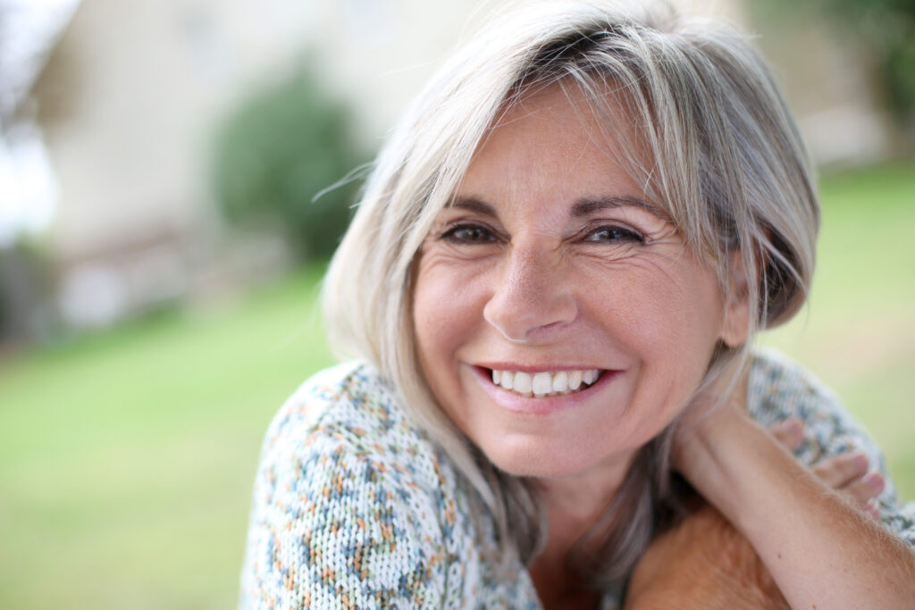Smiling mature woman enjoying a relaxed outdoor moment, embodying hormonal wellness achieved with acupuncture.