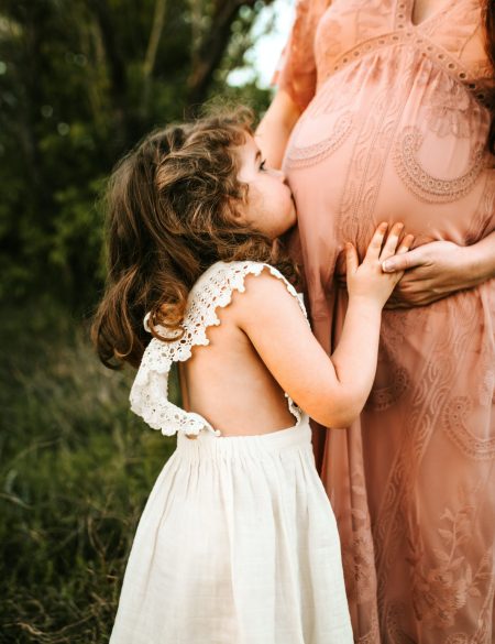 Little girl kissing her pregnant mother's belly, a tender moment of anticipation for a new sibling, supported by acupuncture for fertility.