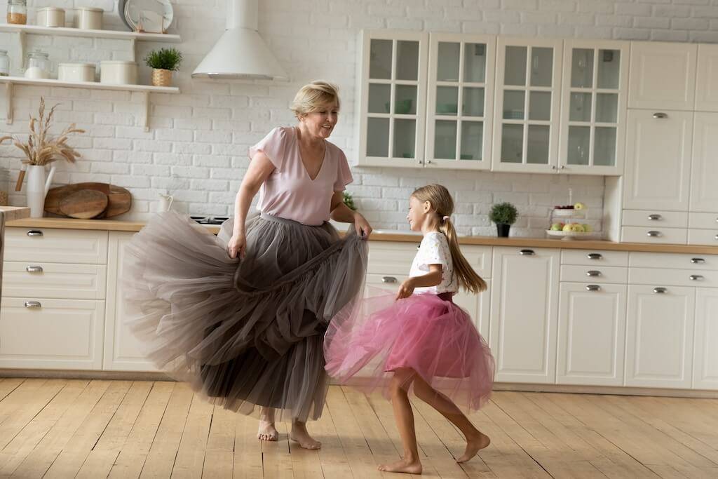 Grandmother and granddaughter twirling in tutus in a bright kitchen, celebrating movement and freedom from neuropathy.