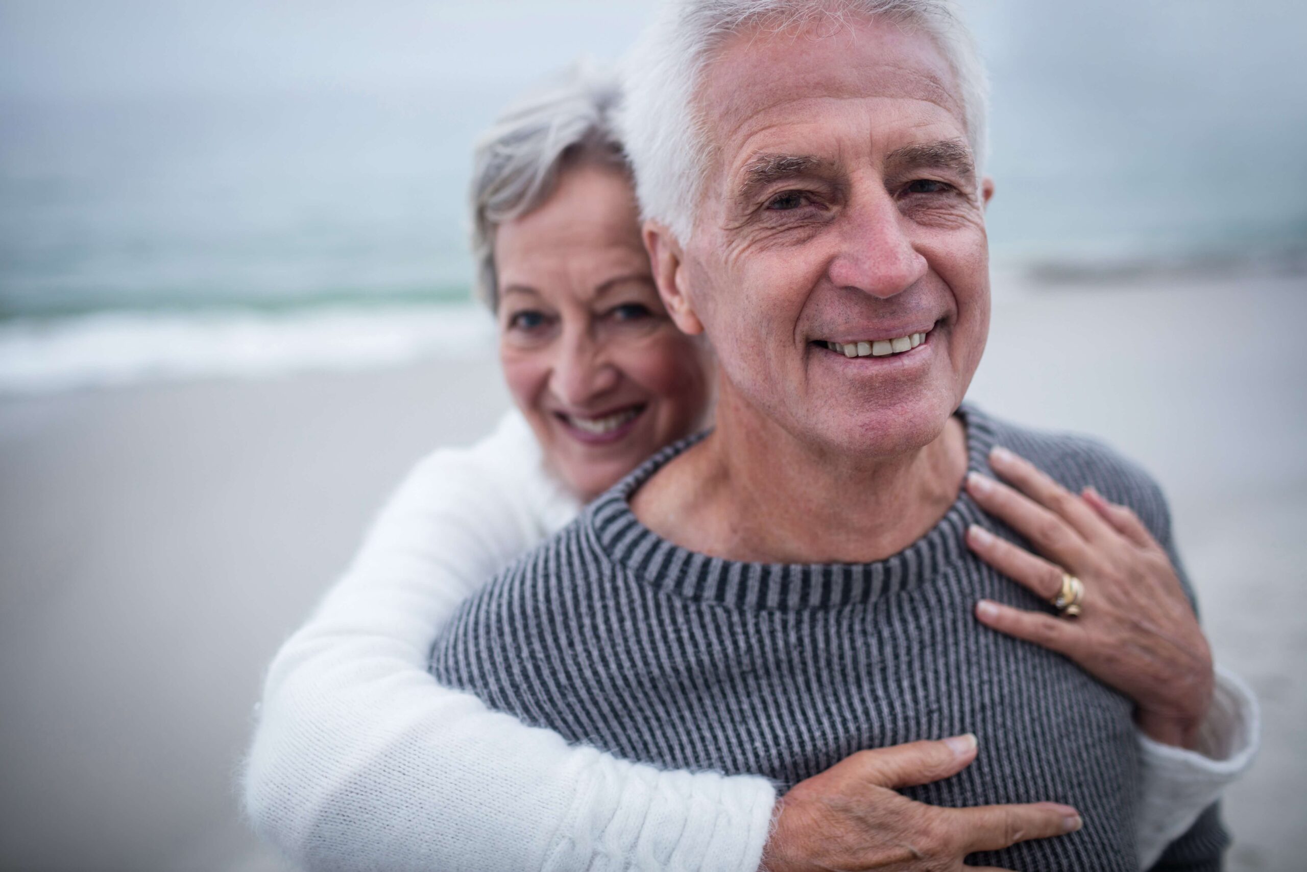 This photo captures a tender moment between a senior couple on the beach, symbolizing their continued enjoyment of life's simple pleasures, unhindered by neuropathic pain, thanks to the supportive role of acupuncture in their health regimen.